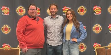 Three people posing in front of a professional fire fighters backdrop.