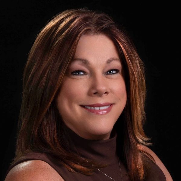 Smiling woman with shoulder-length brown hair and a dark top against a black background.