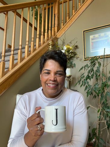 Smiling woman holding a white mug with the letter J in a cozy home setting.