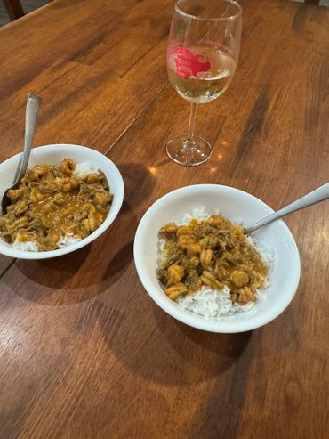 Two bowls of shrimp stew over rice with a glass of white wine on a wooden table.