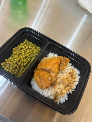 Meal with cooked peas, seasoned chicken, and white rice in a black divided container.