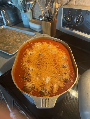 A pot of meatballs in tomato sauce topped with grated cheese on a stove.