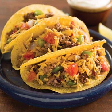 Three tacos filled with seasoned ground beef, rice, tomatoes, and green bell peppers on a blue plate.