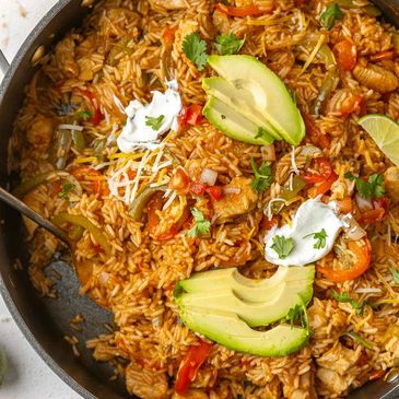 A skillet of Mexican rice with chicken, avocado slices, and sour cream.