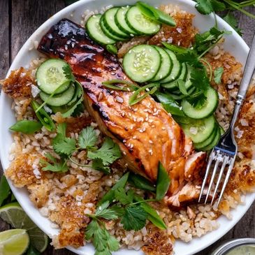 Grilled salmon with crispy rice, cucumber slices, and fresh herbs in a bowl.