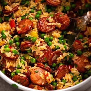 Fried rice with peas and sliced sausages in a pan.
