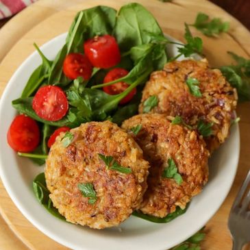 Three golden-brown patties with fresh greens and cherry tomatoes on a white plate.