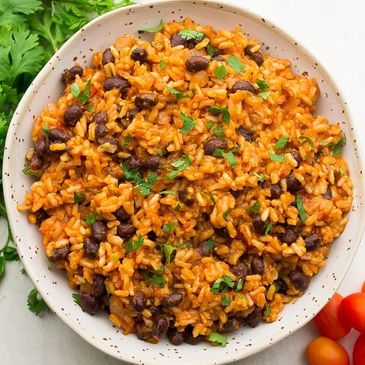 A bowl of seasoned rice with black beans garnished with fresh herbs.