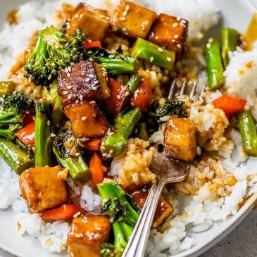 Tofu stir-fry with broccoli, carrots, and rice topped with sesame seeds.