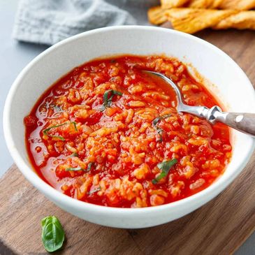 A bowl of tomato rice soup garnished with basil and a spoon inside.