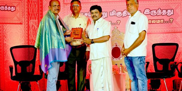 Four men at an award ceremony, one receiving a plaque while draped in a shawl.