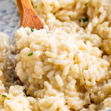 Creamy cheesy risotto being stirred with a wooden spoon.