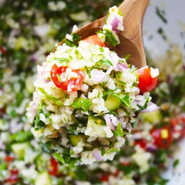 Fresh tabbouleh salad with parsley, tomatoes, and onions on a wooden spoon.