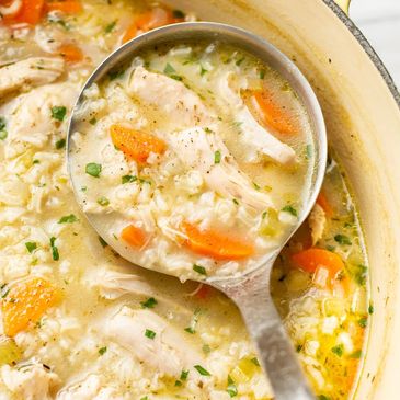 A ladle of chicken and rice soup with carrots and herbs.