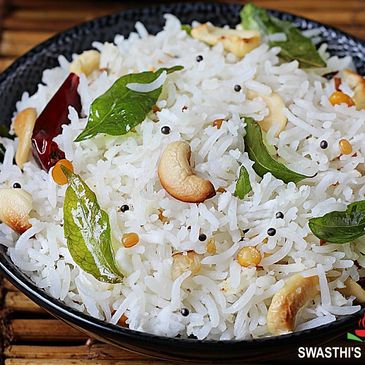 A bowl of coconut rice garnished with cashews, curry leaves, and spices.