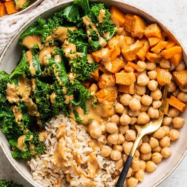 Healthy bowl with kale, chickpeas, rice, roasted sweet potatoes, and dressing.