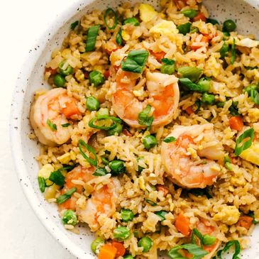 Shrimp fried rice with vegetables and scallions served in speckled bowls.