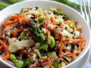A colorful bowl of vegetable rice salad with asparagus and carrots.