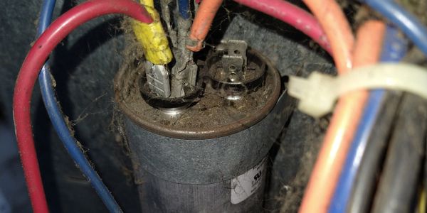 Close-up of a dusty electrical capacitor with wires connected.