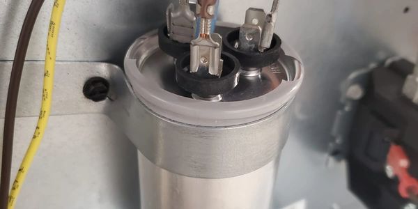 Close-up of an electrical capacitor inside a metal panel.