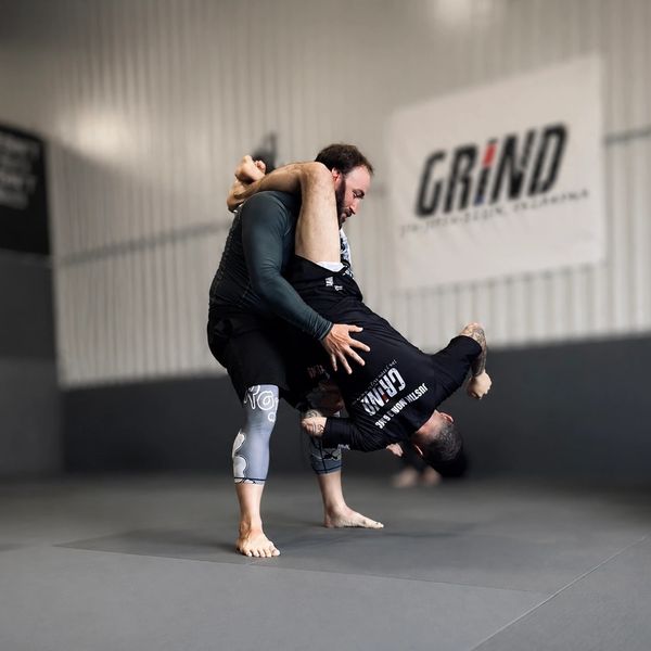Two men practicing Brazilian Jiu-Jitsu grappling techniques in a gym.