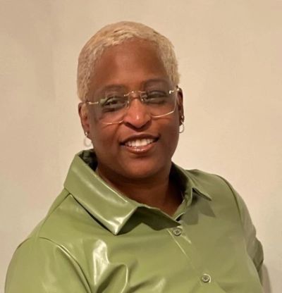 Person smiling wearing glasses and a green leather jacket.