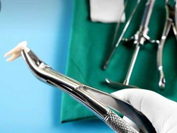 Dental extraction forceps holding a tooth with surgical tools in the background.