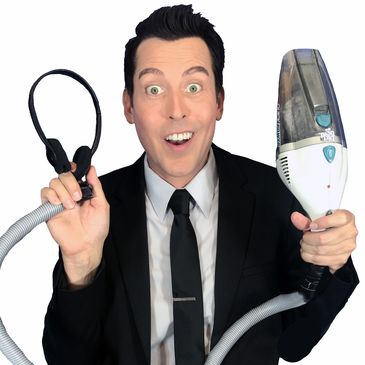 Man in suit holding a vacuum hose and headset, smiling widely.