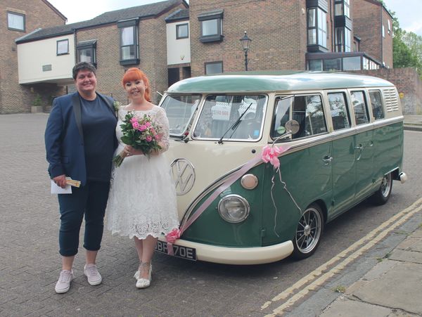 Two women getting married, stood by a green and white VW van smiling.