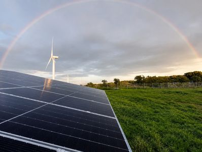 Solar panels and wind turbines under a rainbow.