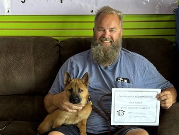 David, a military veteran, seated with his service dog Buck while holding a certificate of accomplis