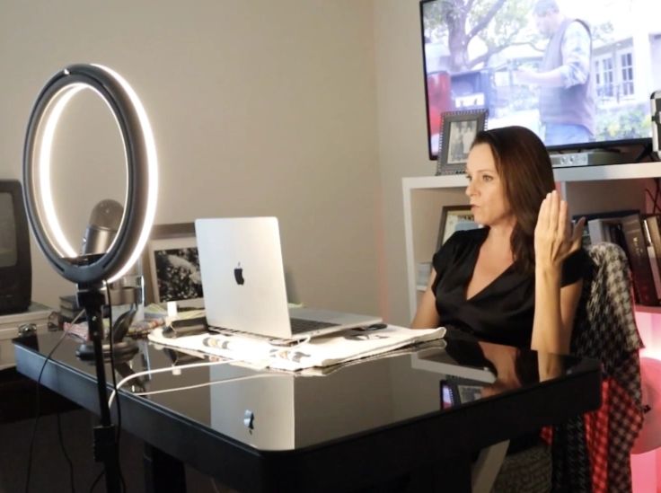 Woman in video call setup with ring light and laptop at desk.