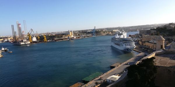 Large ship docked at a busy harbor with cranes and buildings.