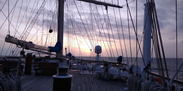 Sailboat deck at sunset with ocean and sky.