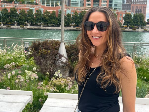 Woman smiling near a waterfront with flowers and buildings in the background.