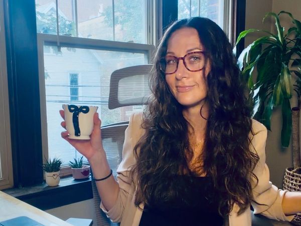 Woman with glasses holding a cup and smiling.