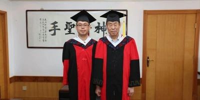 Two graduates in black and red gowns standing indoors.