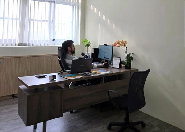 Man working on a computer in a modern office with plants and a laptop.