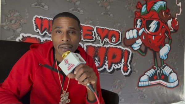 Man in red hoodie holding a microphone with colorful cartoon background.