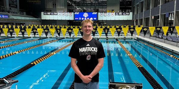 Young male swimmer stands by indoor pool with empty lanes.