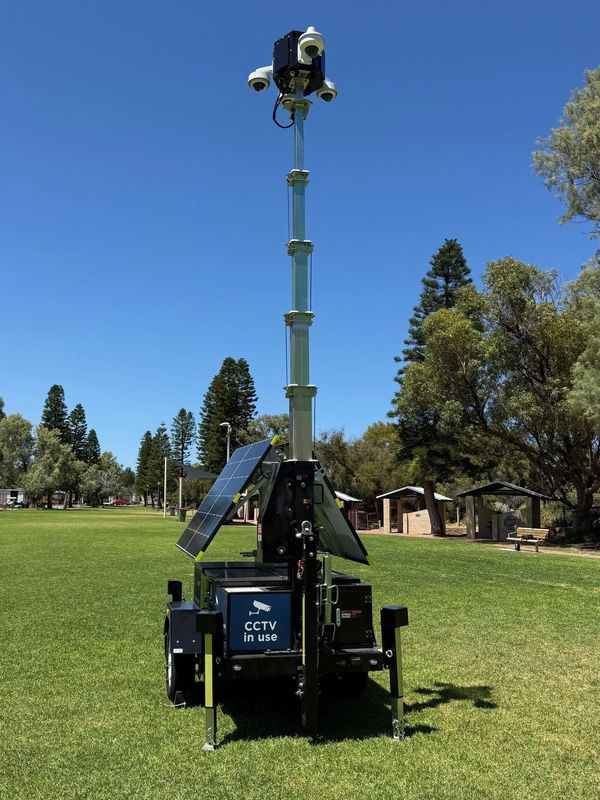 Mobile CCTV tower with solar panels in a park under clear blue sky.