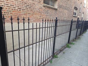 Black wrought iron fence along a city sidewalk beside a brick building.