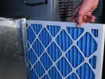 A hand replacing a blue air filter in an HVAC system.