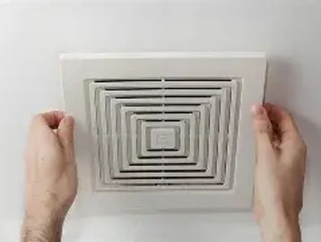 Hands adjusting a square ceiling air vent grille.