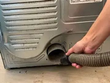 Hand cleaning a washing machine drain hose with a vacuum.
