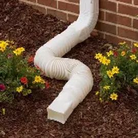 White flexible downspout extension directing water away from a brick wall.