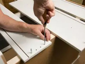 Person assembling white furniture using a screwdriver.