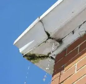 Cracked gutter with water leaking down the side of a brick building.