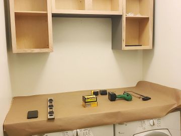A laundry area with shelves and tools on a covered countertop.