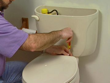 Person fixing a toilet with a screwdriver.